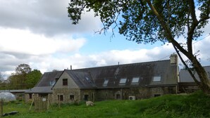 A stone building with multiple windows and a sloped roof, surrounded by greenery.