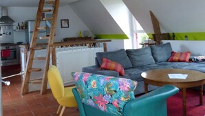 A loft-style room with a sloped ceiling, a wooden ladder, a sofa, a chair, and a table.