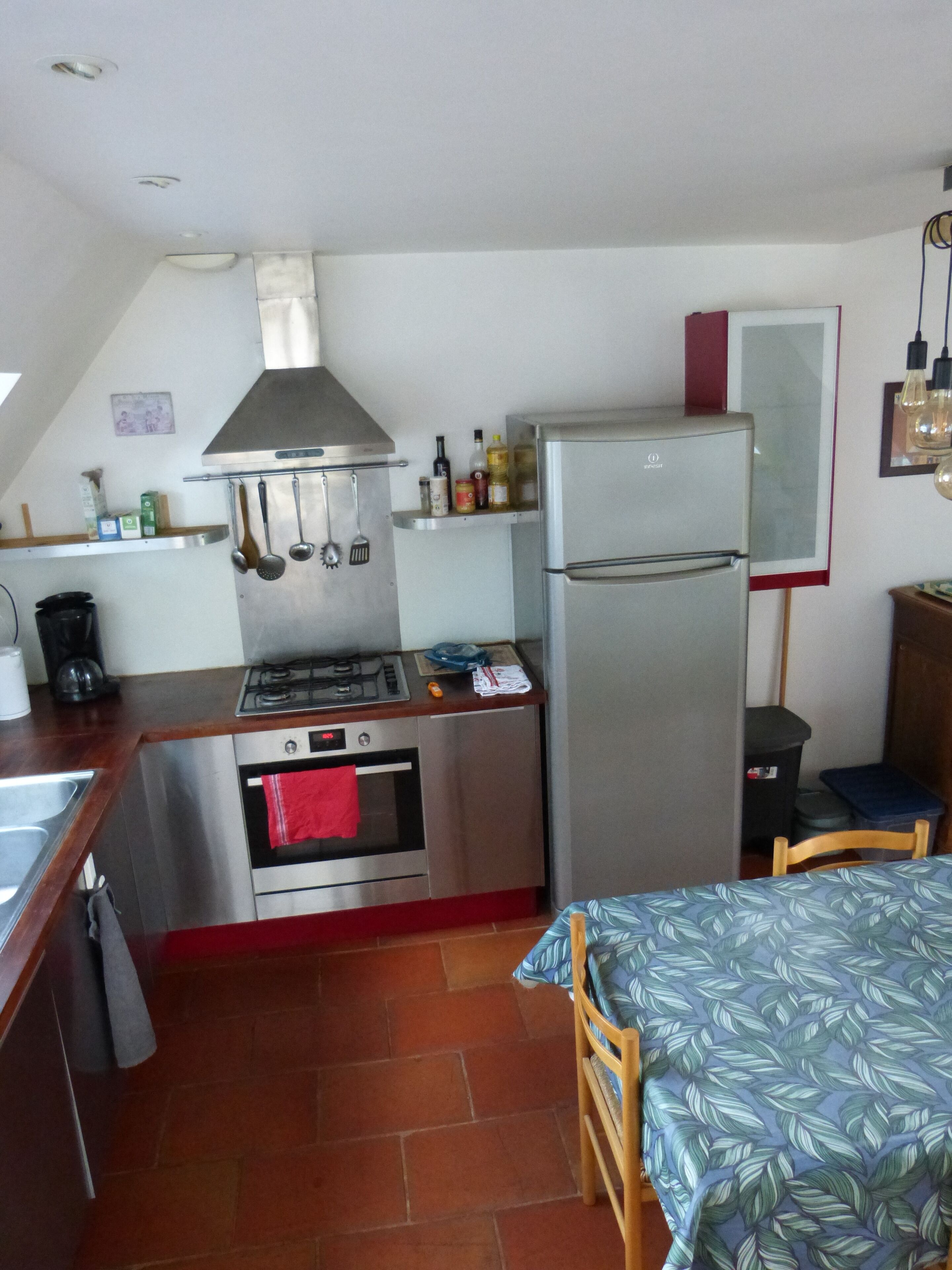 A compact kitchen with a stove, oven, and refrigerator, a small dining area with a table, and a tiled floor.