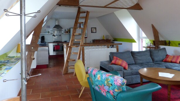A loft-style room with a kitchen, a dining area, and a living space with a sofa and chairs.