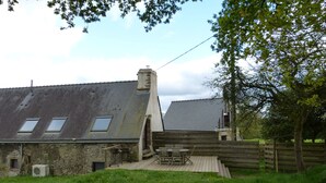 A rustic stone building with a sloped roof, a wooden deck, and a small outdoor seating area.