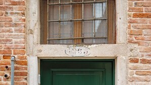 Eine grüne Tür mit Metallriegel, ein kleines Fenster mit Metallgitter und eine Ziegelwand.