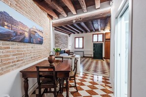 A dining area with a brick wall, wooden ceiling beams, a checkered floor, and a view of a cityscape through a window. - GDL HOUSE VENICE (Venezia)