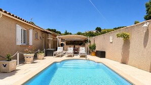 Une piscine avec des chaises longues, un patio couvert et un mur en pierre.