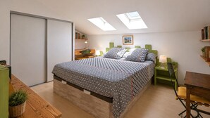 Une chambre à coucher comprenant un lit, un bureau, une chaise, une bibliothèque et des fenêtres de toit.