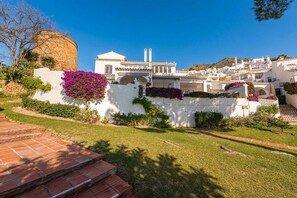 Un edificio blanco con un muro de piedra, escalones que lo conducen y un cielo azul despejado.
