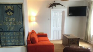 A living room with a red sofa, a brown armchair, a wooden coffee table, a wall-mounted TV, and a door. - New beach front sea view apartment superking or twin. Featured in Netflix series (Deal)