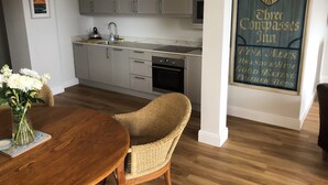 A modern kitchen with white cabinets, a dining table with a vase of flowers, and a wall-mounted sign. - New beach front sea view apartment superking or twin. Featured in Netflix series (Deal)