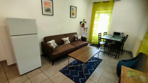 Un espace de vie compact comprenant un coin cuisine, un canapé agrémenté de coussins à motifs, une table à manger avec des chaises et une petite plante en pot.