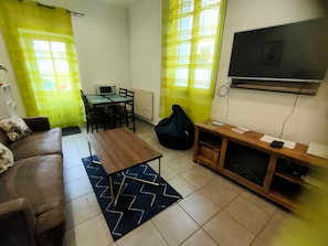 A living room with a sofa, a coffee table, a TV, a small table with a chair, and a bean bag. - Apartment “La Coquille” with Private Terrace and Wi-Fi (Moissac)