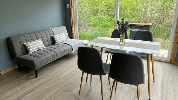 Ein modernes Wohnzimmer mit einem grauen Sofa, einem weißen Esstisch und schwarzen Stühlen.