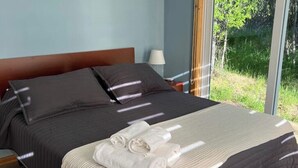 Ein Bett mit dunklem Kopfteil, einem weißen Handtuch und Blick ins Grüne.