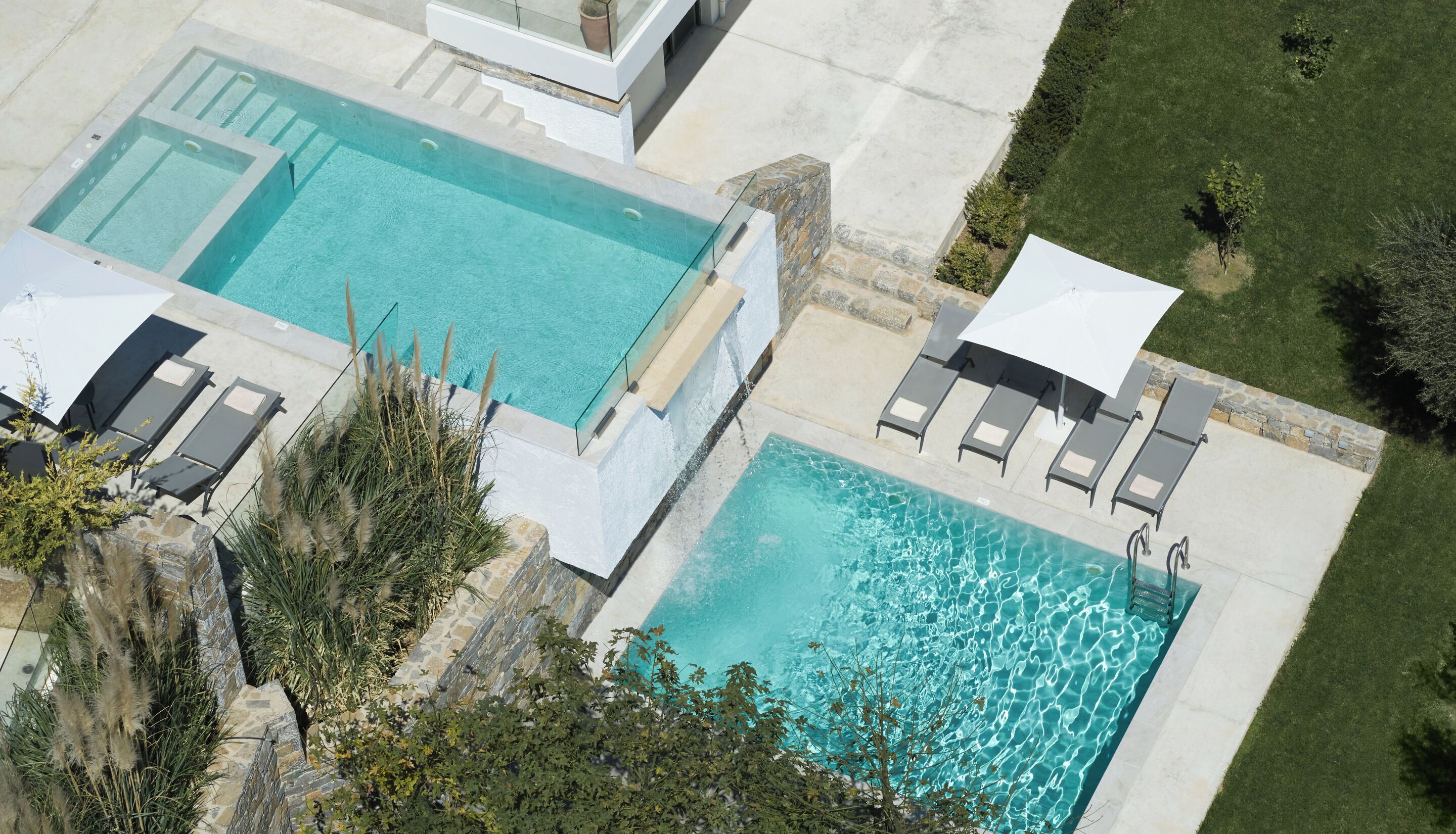 A rectangular swimming pool with a stone border, adjacent lounge chairs, and a small garden area.