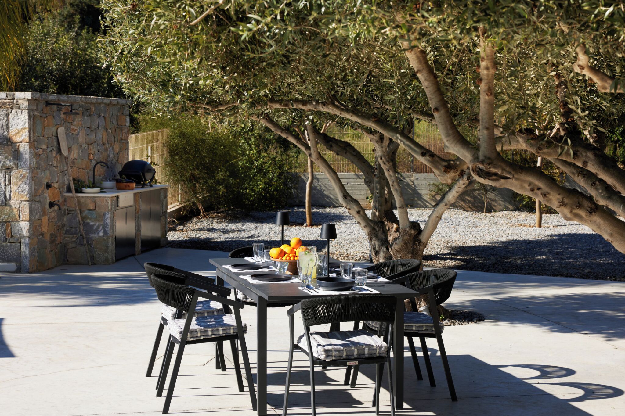 An outdoor dining area with a stone-built grill, a table set for four, and chairs.