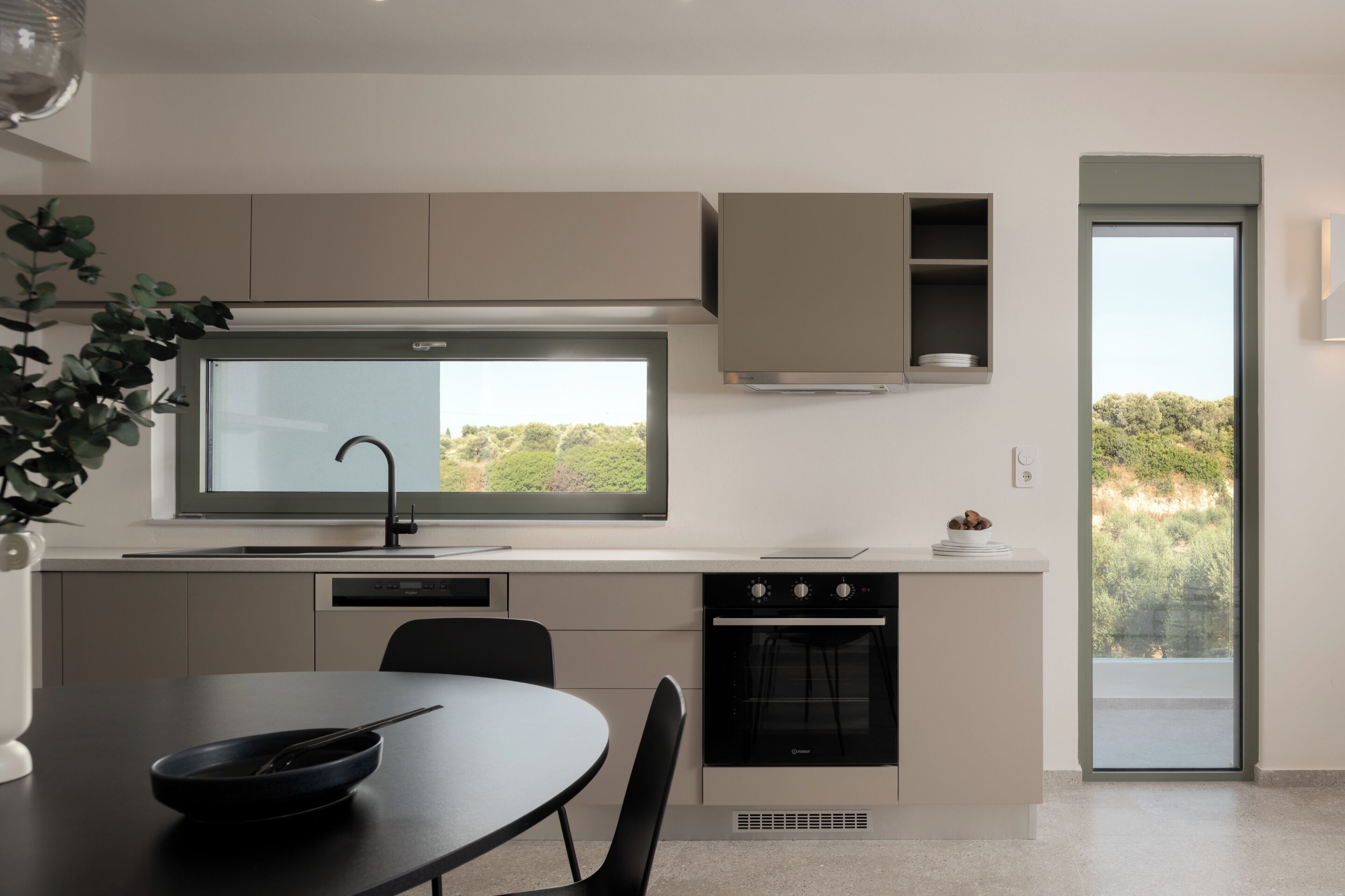 A modern kitchen with a large window, built-in oven, and a dining area with a table and chairs.