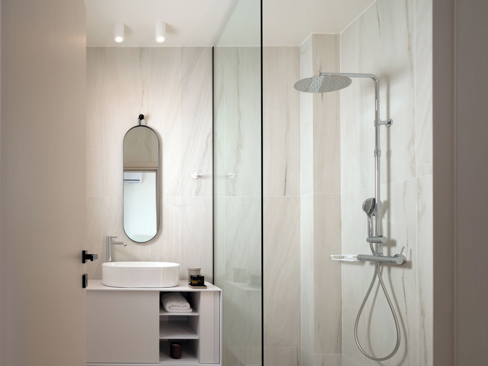 Een moderne badkamer met een witte wastafel, een spiegel, een douche met handdouche en een douchecabine met glazen wanden.