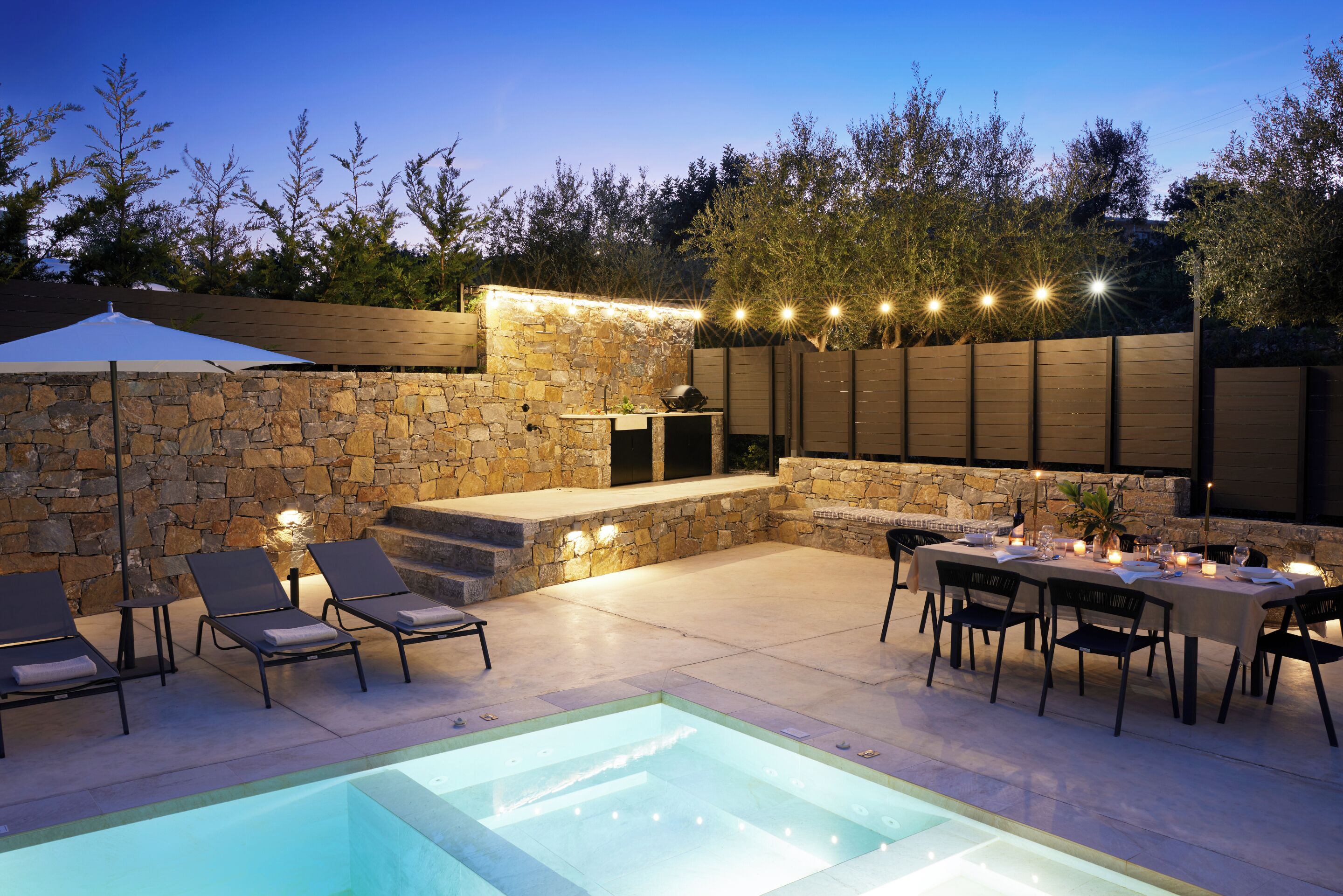 Patio esterno con piscina, pareti in pietra e zona pranzo con sedie e tavolo.