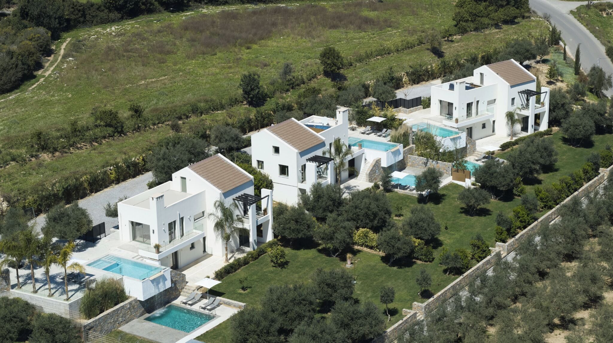 Un complexe résidentiel moderne comprenant plusieurs maisons, chacune dotée d’une piscine et d’un jardin bien entretenu.