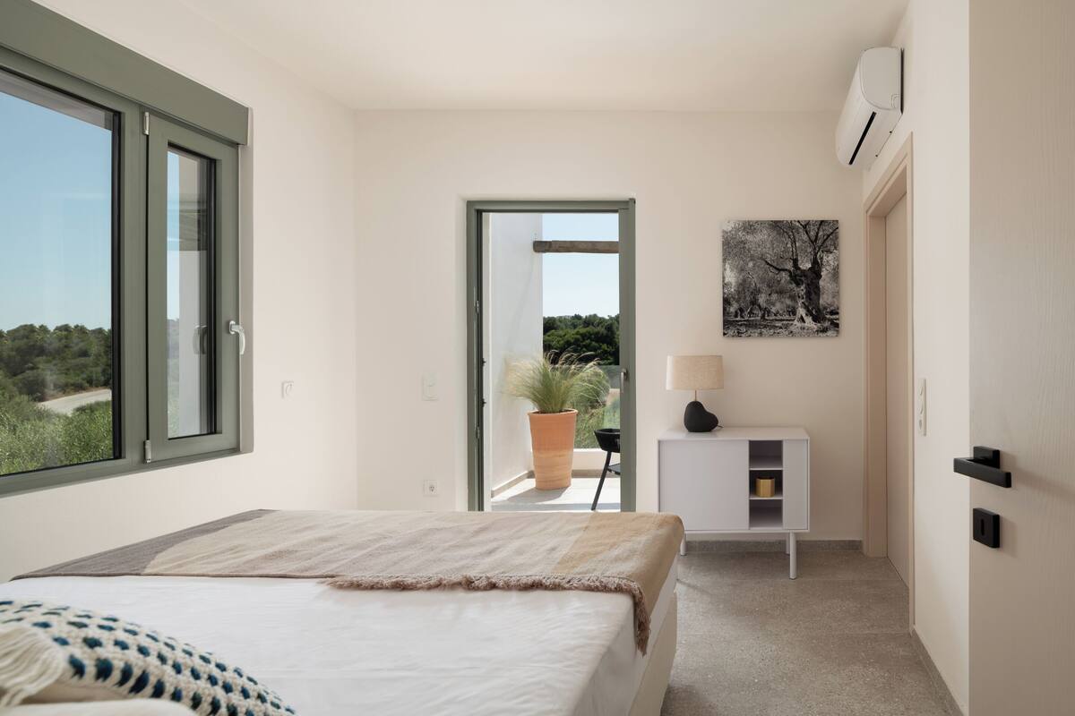A bedroom with a bed, a potted plant, a desk, and a window.