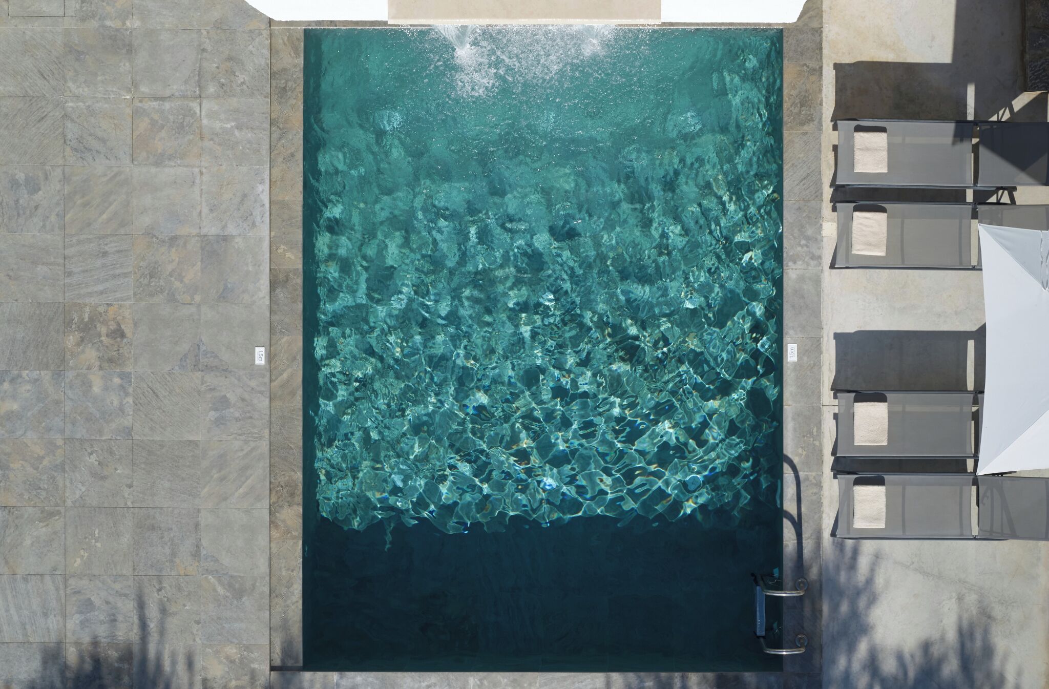 Ein großer rechteckiger Pool mit klarem Wasser, umgeben von Steinfliesen und Sitzmöglichkeiten im Freien.