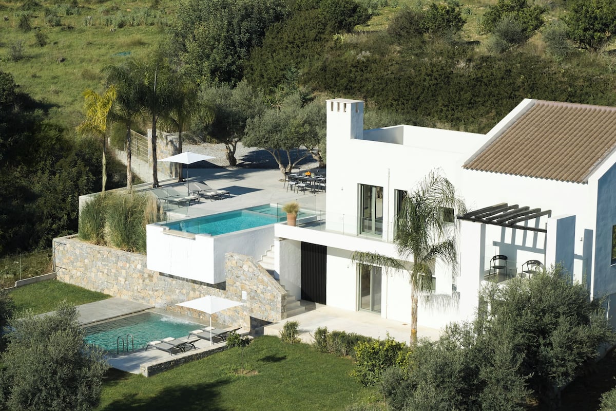 A modern house with a swimming pool, outdoor seating, and a stone wall.