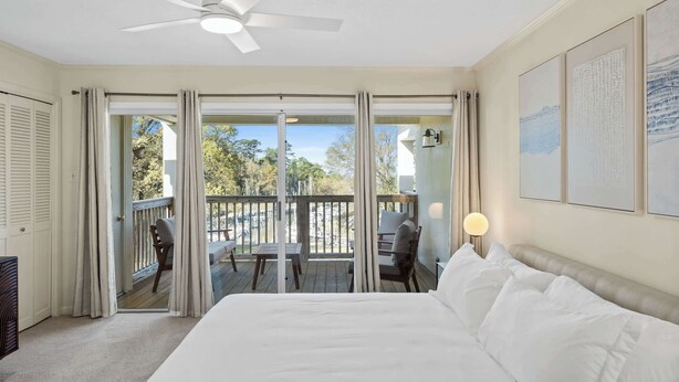 A bedroom with a bed, a ceiling fan, a balcony with a table and chairs, and a view of the outdoors. - Fly Creek Collection - Sunset Perch (Fairhope)