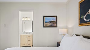 A hotel room with a bed, a dresser, a mirror with lights, a framed painting, and a lamp. - Fly Creek Collection - Sunset Perch (Fairhope)