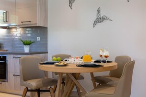 Eine moderne Küche mit Essbereich, ausgestattet mit einem runden Holztisch für vier Personen, einem Topf mit Pflanze und einem an der Wand befestigten Vogelkunstwerk.