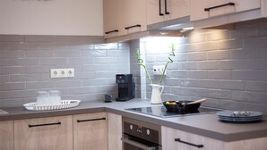 Una cocina moderna con armarios de madera clara, salpicadero de azulejos grises, una cafetera y un florero con plantas verdes.