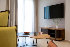 Ein modernes Hotelzimmer mit einem gelben Sessel, einem kleinen runden Tisch mit einer Schüssel Müsli und zwei Tassen, einem Holz-Konsolentisch mit einem Fernseher darüber und einem Fenster mit Vorhängen.