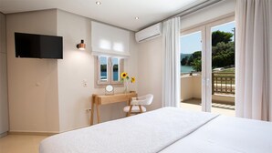 Un dormitorio con cama, escritorio, silla, televisor y balcón con vistas.