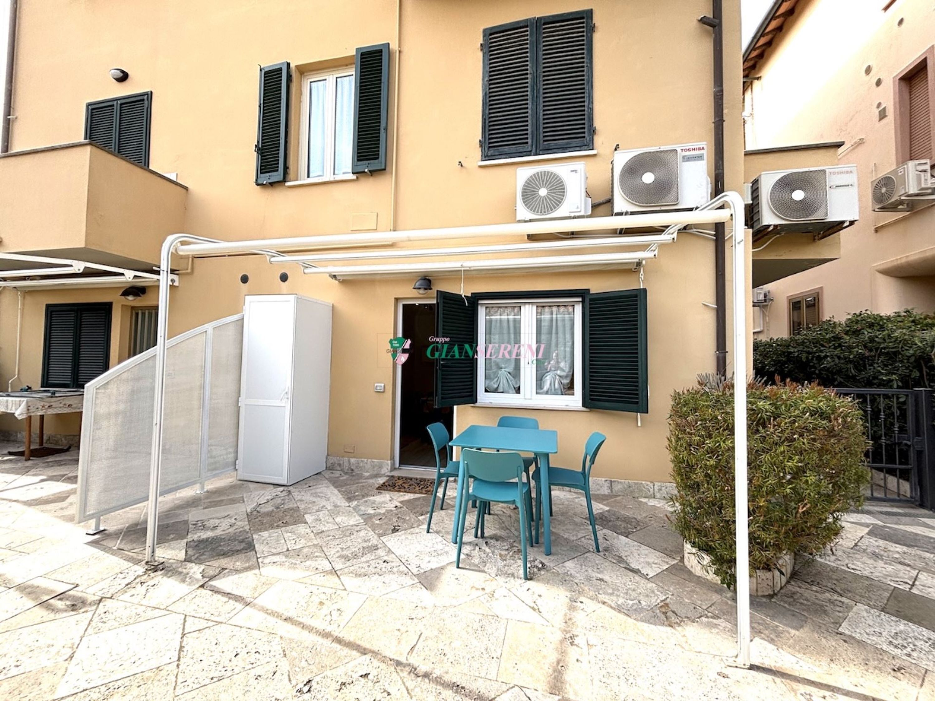 Un bâtiment équipé de climatiseurs, doté d’un espace extérieur couvert avec des tables et des chaises, et dont la porte porte l’inscription « Gruppo GIANIERI ».