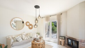 Een woonkamer met een bank, een rond bijzettafeltje, een open haard en grote ramen.