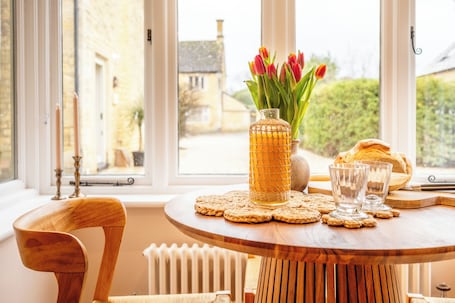 A wooden table with a vase of tulips, two glasses, and a loaf of bread.