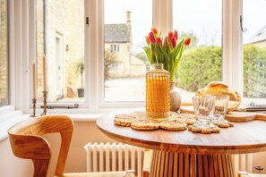 A wooden table with a vase of tulips, two glasses, and a loaf of bread. - The Cowshed Banham Cottages (Bourton-on-the-Water)