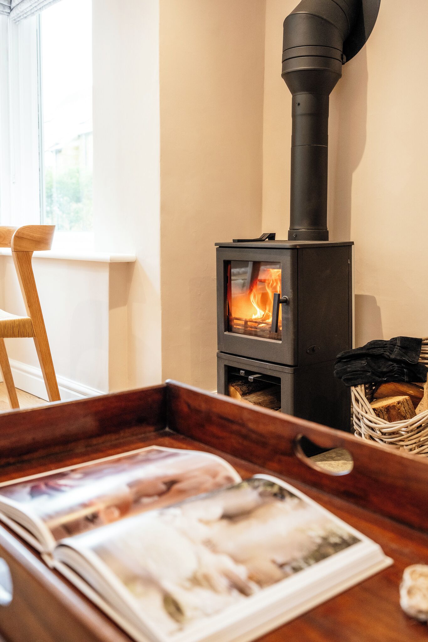 A wood-burning stove with a glass door, a wooden chair, and a magazine on a wooden tray.