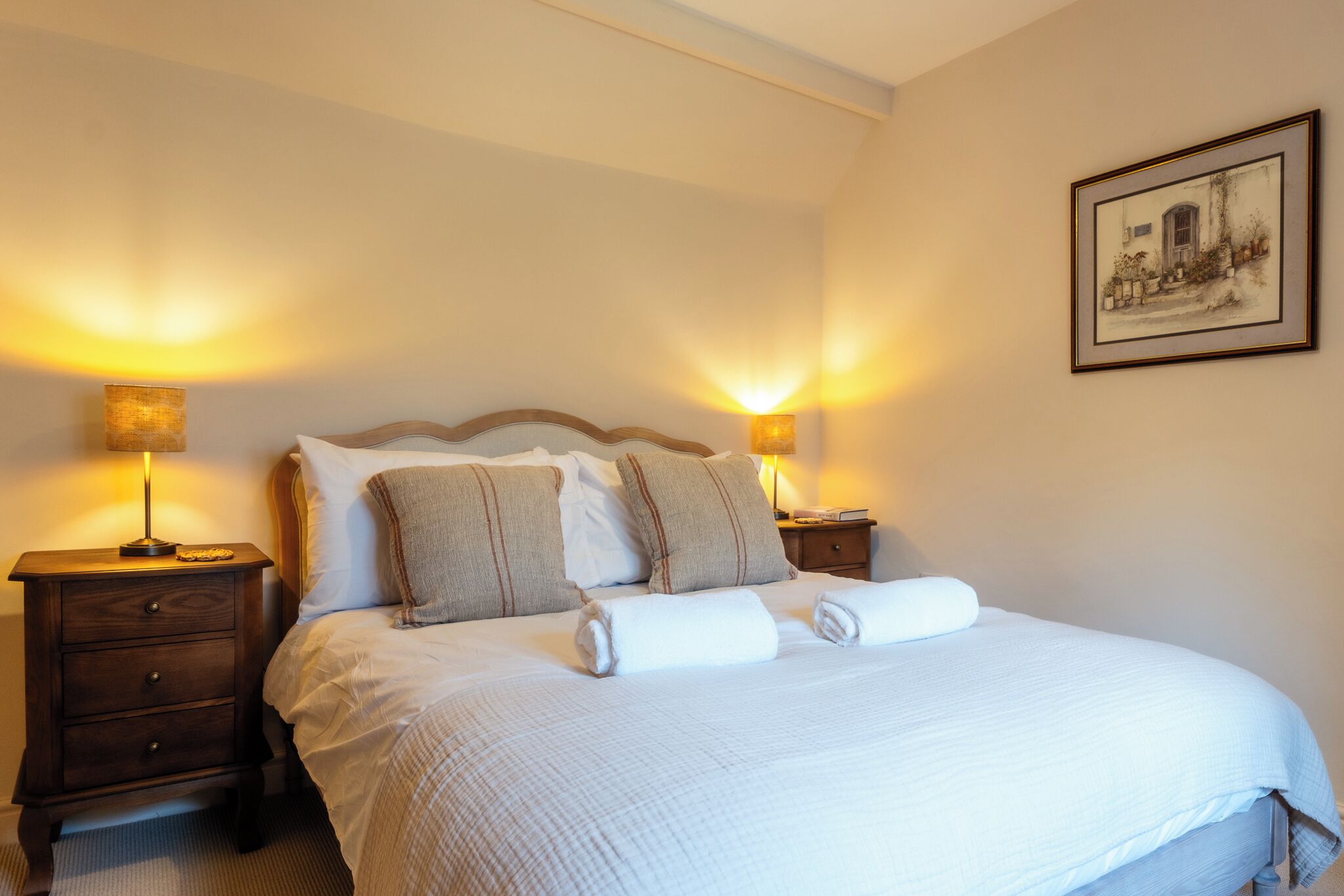 A neatly made bed with pillows and a blanket, two bedside lamps, a nightstand, and a framed picture on the wall.