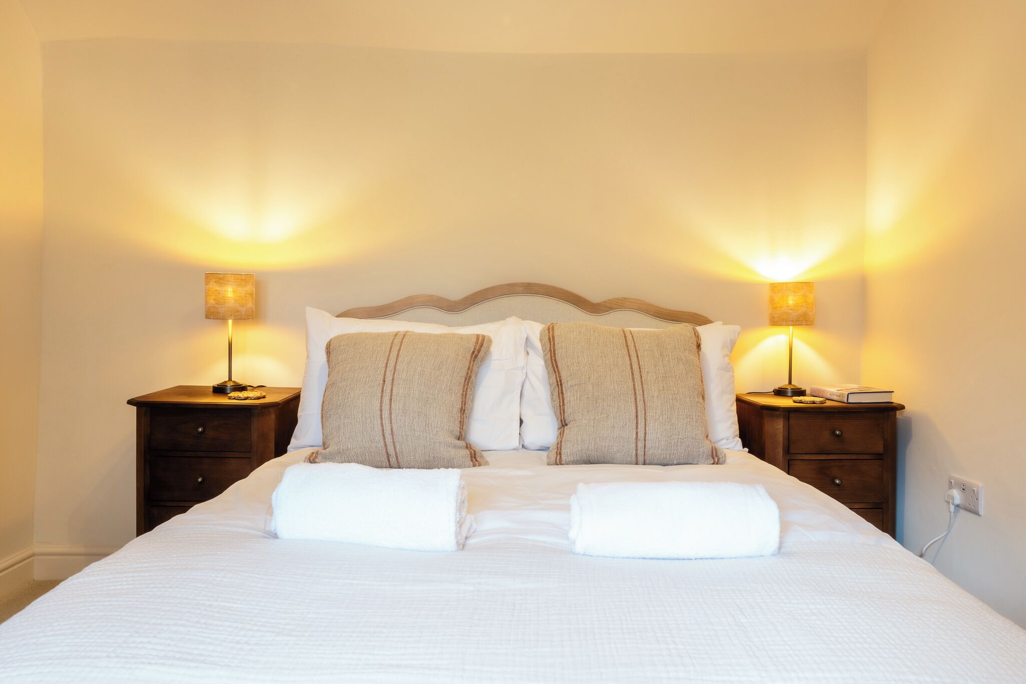 A neatly made bed with pillows and a blanket, two bedside tables with lamps, and a wall socket.
