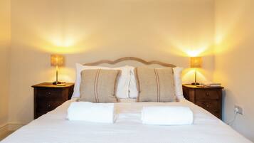 A neatly made bed with pillows and a blanket, two bedside tables with lamps, and a wall socket.