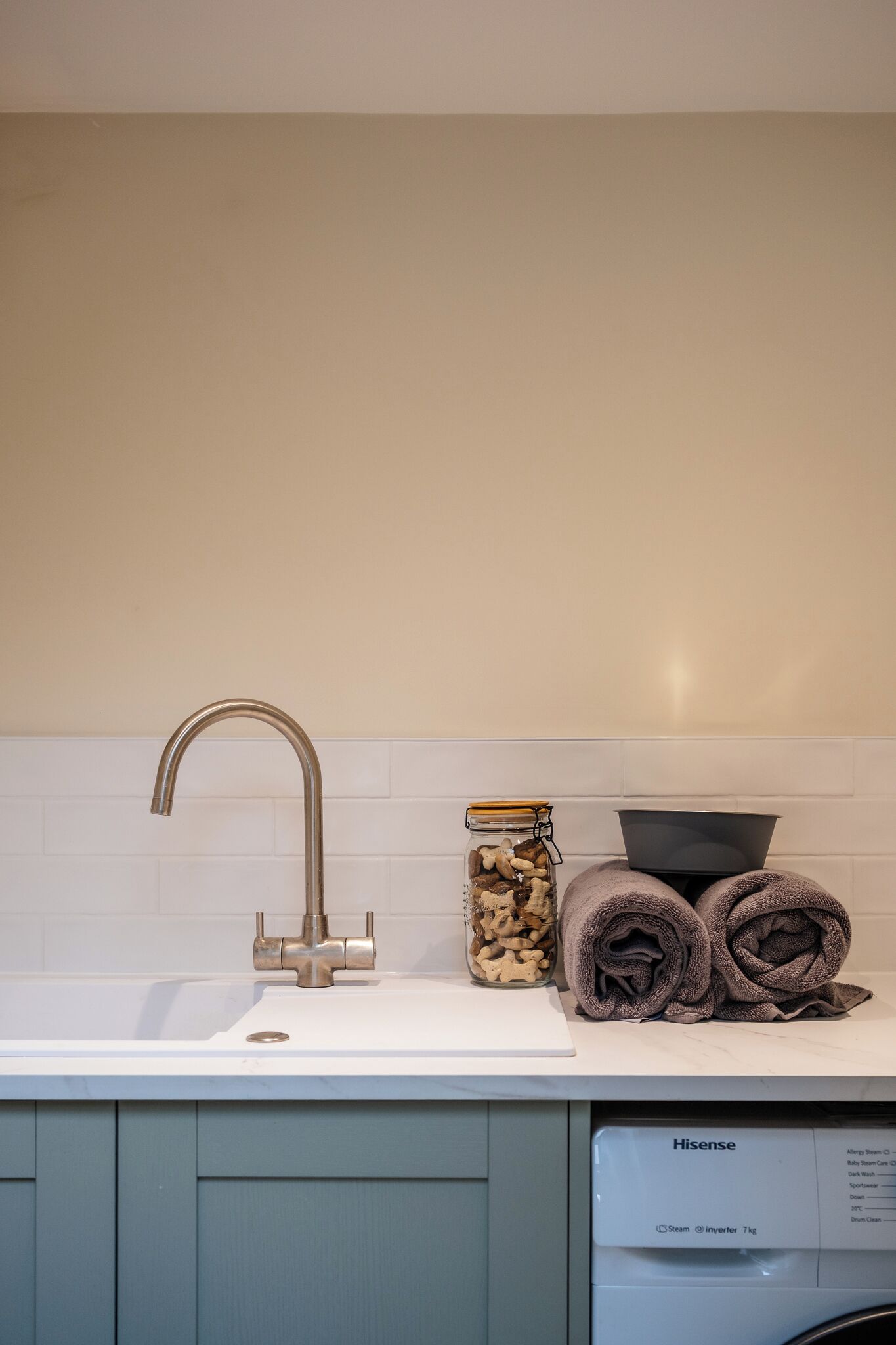 A kitchen with a sink, a faucet, a jar of nuts, and a rolled towel on the counter.