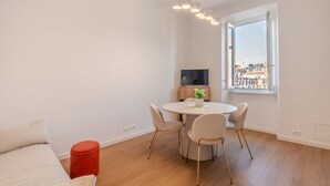Un salon moderne avec une table à manger ronde, un canapé, un pouf rouge, un téléviseur et une fenêtre donnant sur la ville.