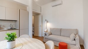 Un salon moderne avec une table ronde, un canapé, un pouf rouge et une plante en pot.