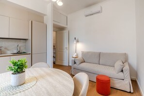 Ein modernes Wohnzimmer mit einem runden Tisch, einer Couch, einem roten Hocker und einer Topfpflanze.