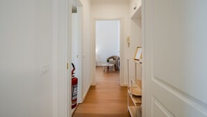 Un couloir avec un extincteur, une chaise et une petite table au fond.