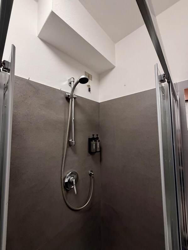 A shower with a handheld showerhead, a wall-mounted faucet, and a handheld shower hose.