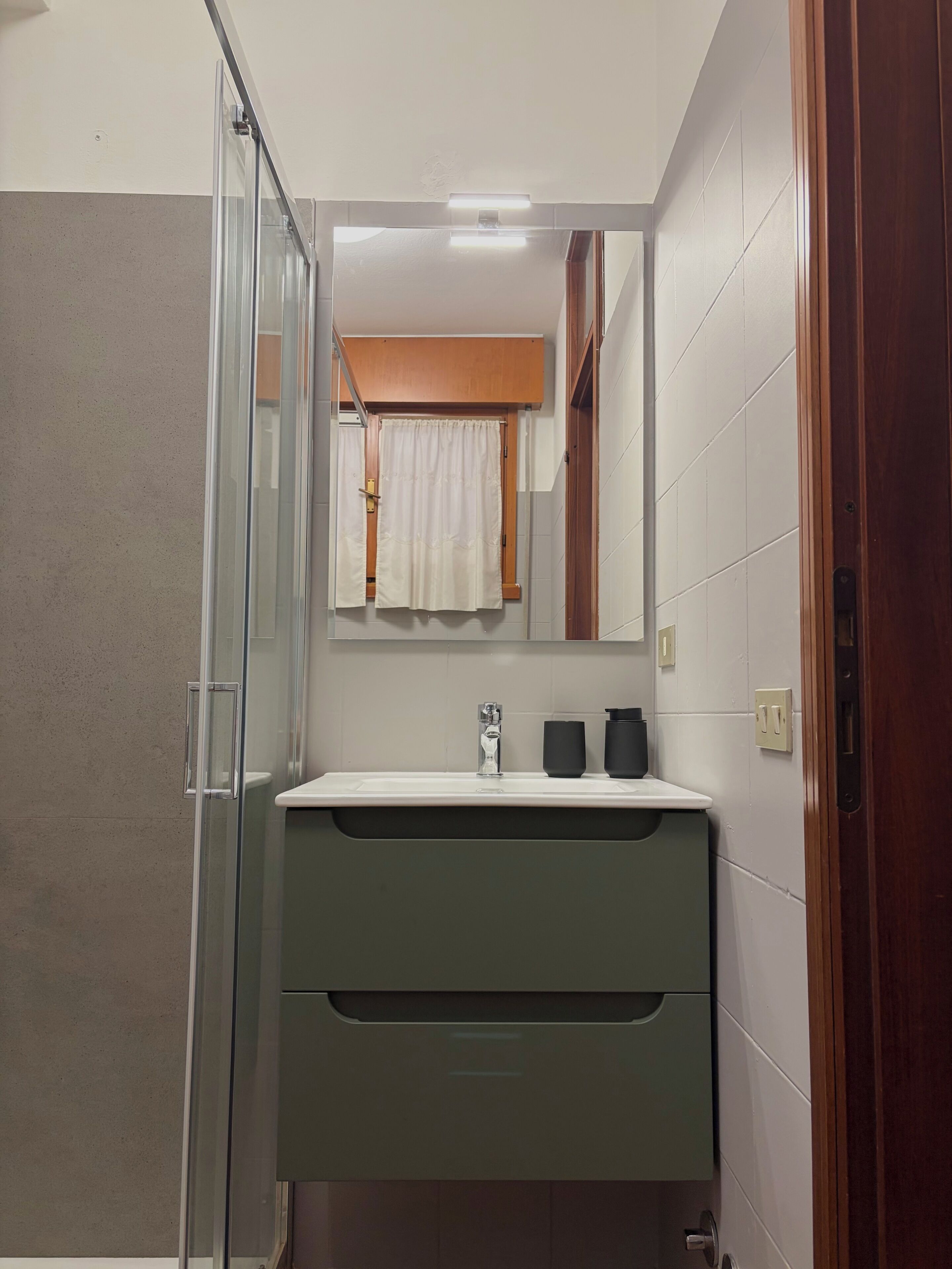 Une salle de bain avec une douche à parois de verre, un lavabo avec un robinet, un miroir au-dessus du lavabo et une serviette accrochée au mur.