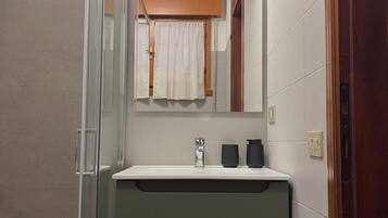 Une salle de bain avec une douche à parois de verre, un lavabo avec un robinet, un miroir au-dessus du lavabo et une serviette accrochée au mur.