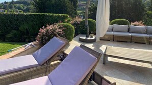 Een terras met rieten lounge fauteuils, een comfortabele bank en een pergola met een witte zonwering.