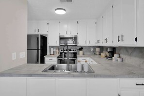 Una cucina moderna con mobili bianchi, elettrodomestici in acciaio inossidabile e un piano di lavoro in granito.