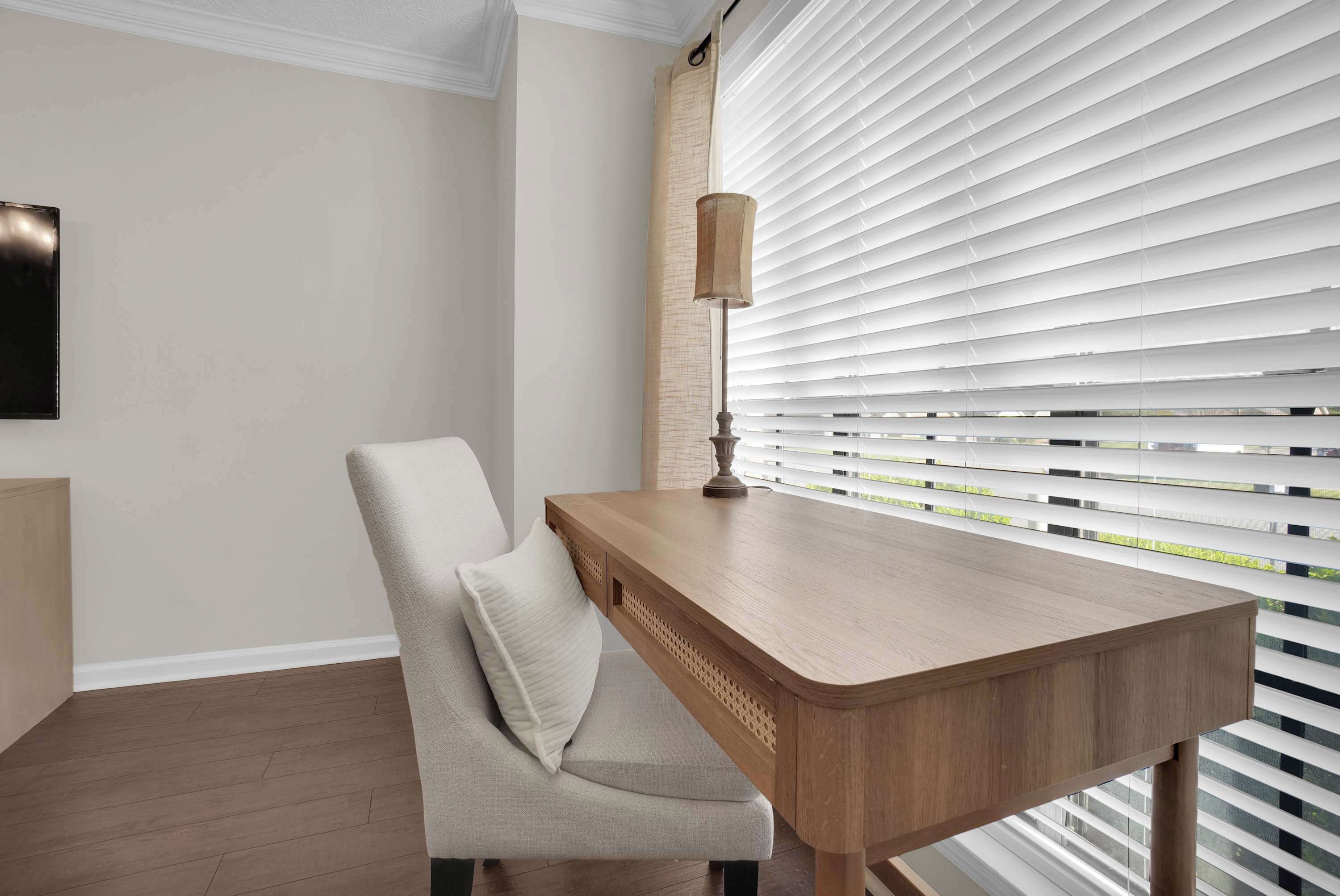 Una habitación con un escritorio de madera, una silla, una lámpara y una ventana con persianas.